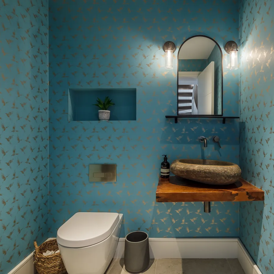 The cloakroom — patterned teal wallpaper and a carved stone basin on a timber shelf