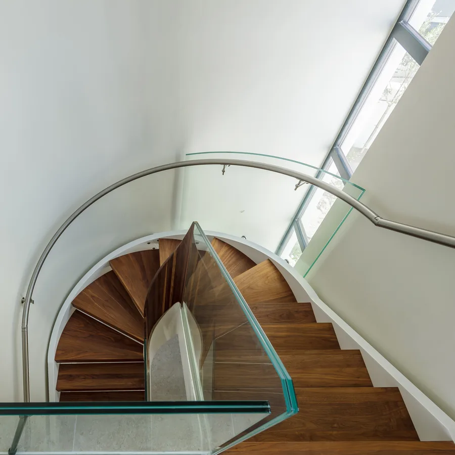 The helical staircase seen from below — walnut treads against a curved white wall