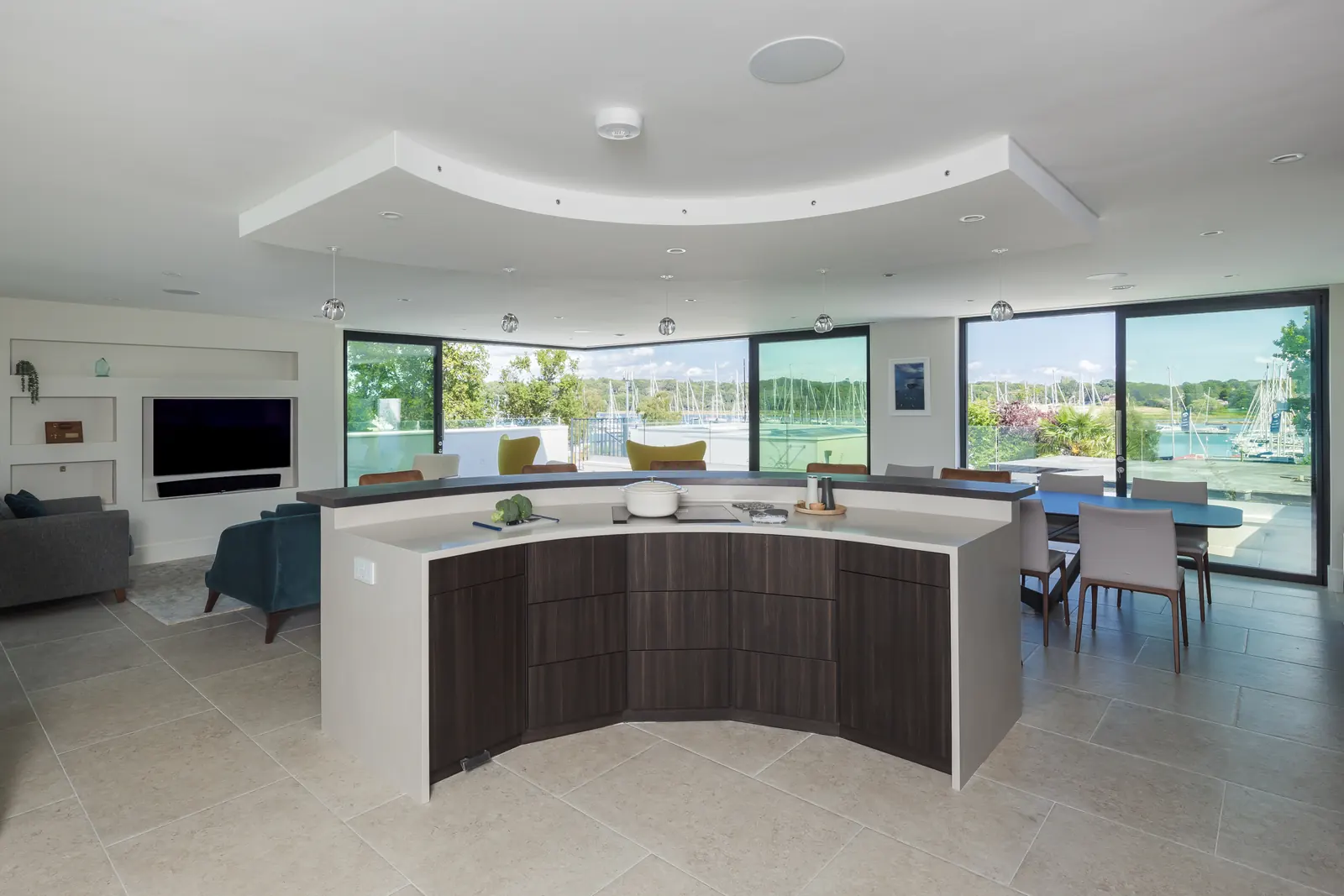 The open-plan first floor: curved kitchen island, lounge seating and dining, with the marina visible through the glazing