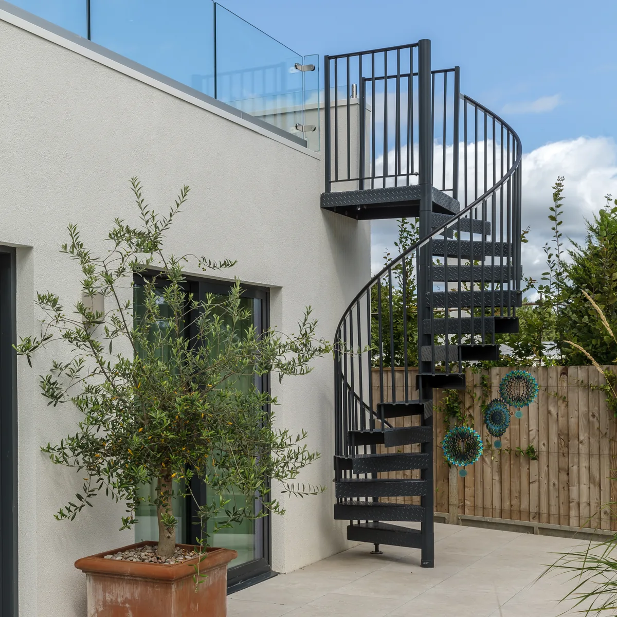 The black spiral staircase against the white render, with an olive tree beside it